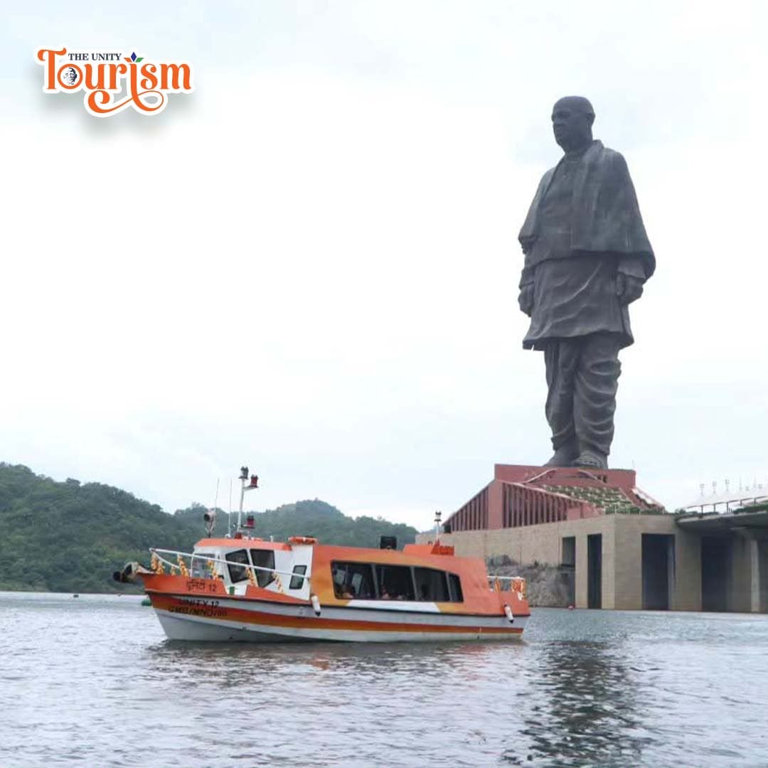 Passenger boat cruising near the Statue of Unity with bridge and hills in the background.