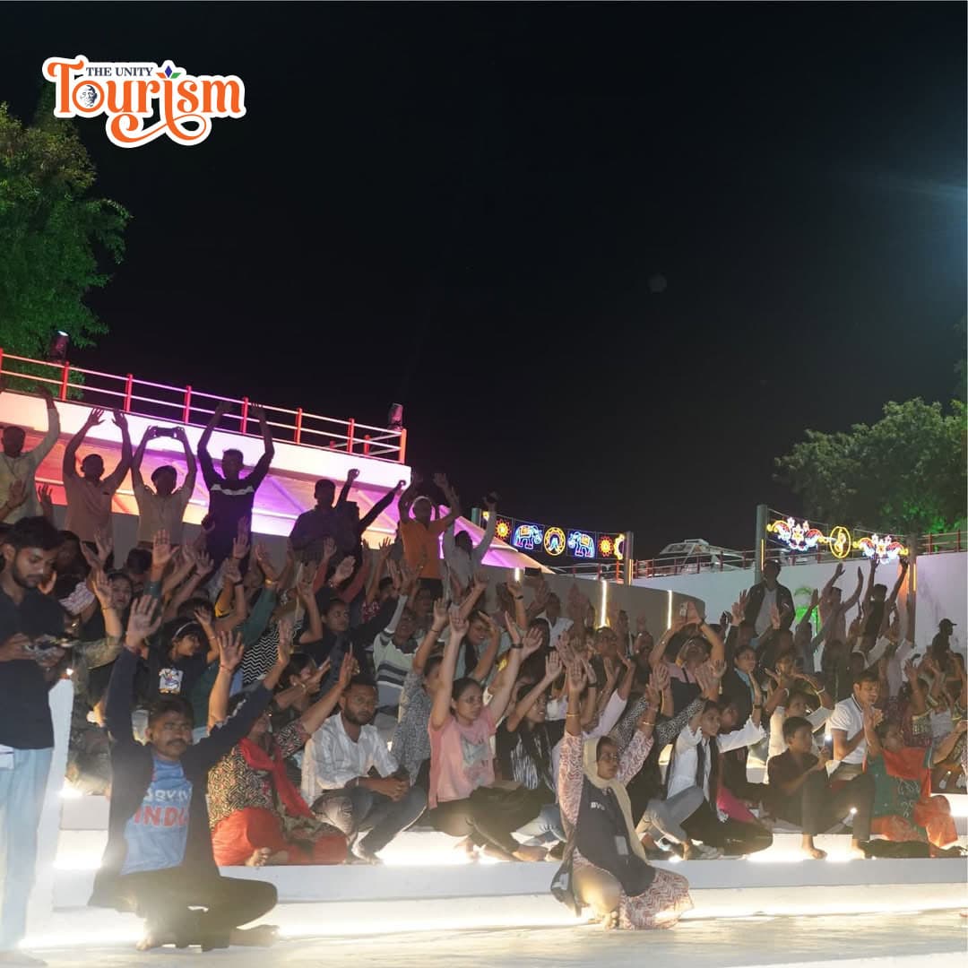 A night scene of individuals seated on steps, celebrating the Pooja at the River Front during the Narmada Maha Aarti.