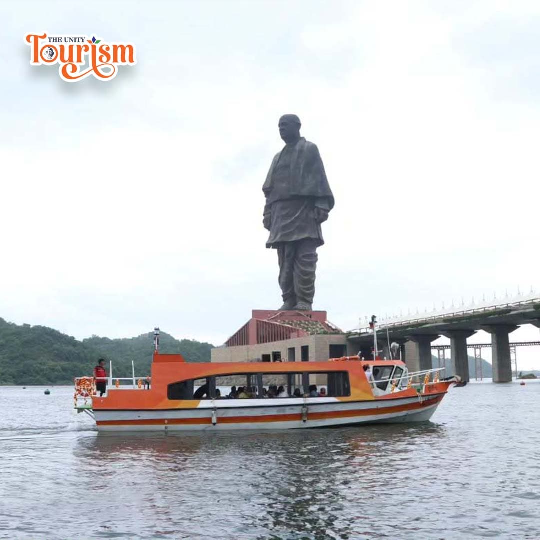 Orange and white tourist boat on Narmada River with Statue of Unity visible in the backdrop.