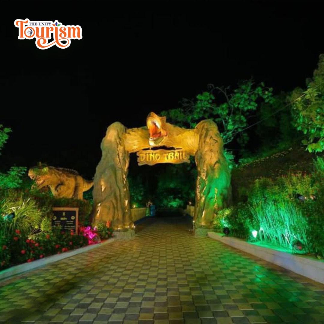 The Night View of entrance to a park showcases a striking dinosaur statue, inviting guests to explore.