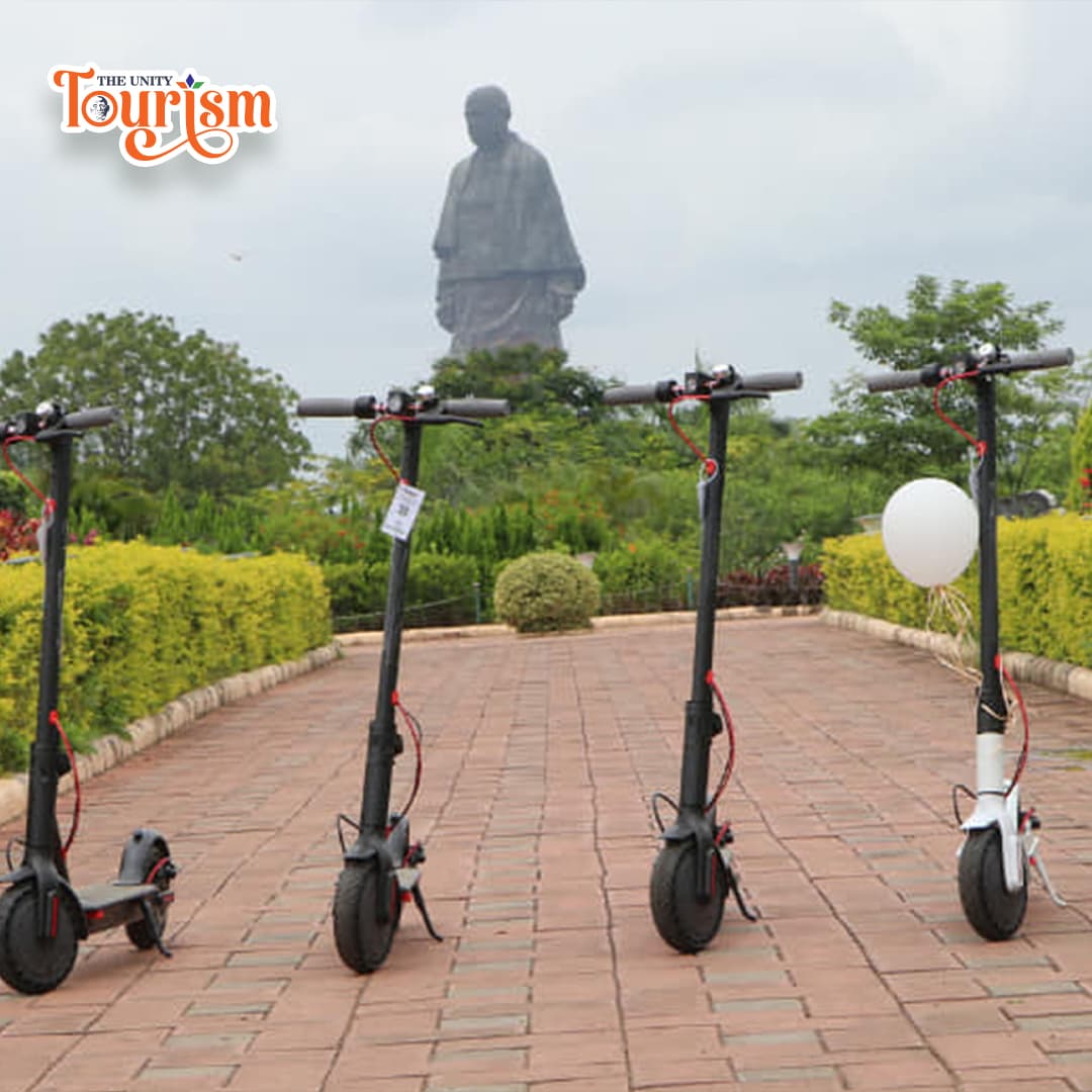 Tourists riding electric kick scooters near Statue of Unity riverfront.