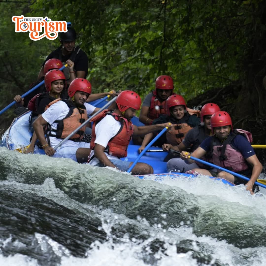 A group of excited individuals wear helmets and life jackets, navigating a white-water rapid in a blue raft surrounded by lush greenery.