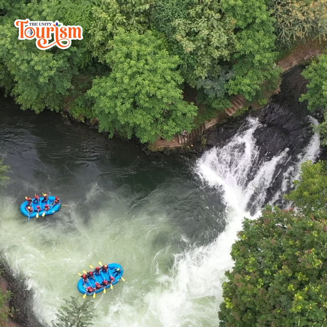Aerial view of two blue rafts navigating a river near a waterfall, surrounded by lush green trees.