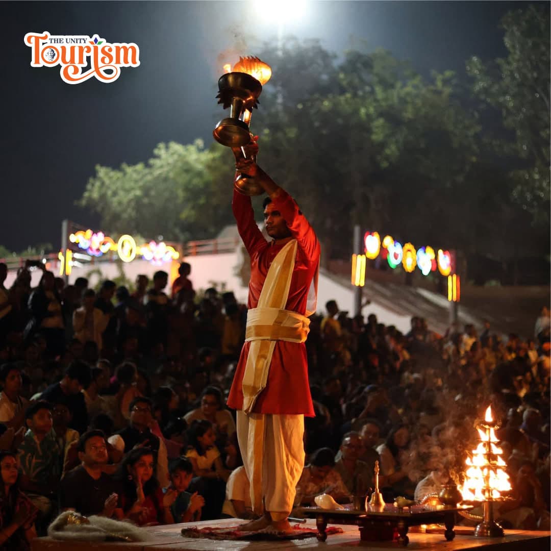 A man dressed in red and white raises a candle while performing Pooja at the riverfront during the Narmada Maha Aarti.
