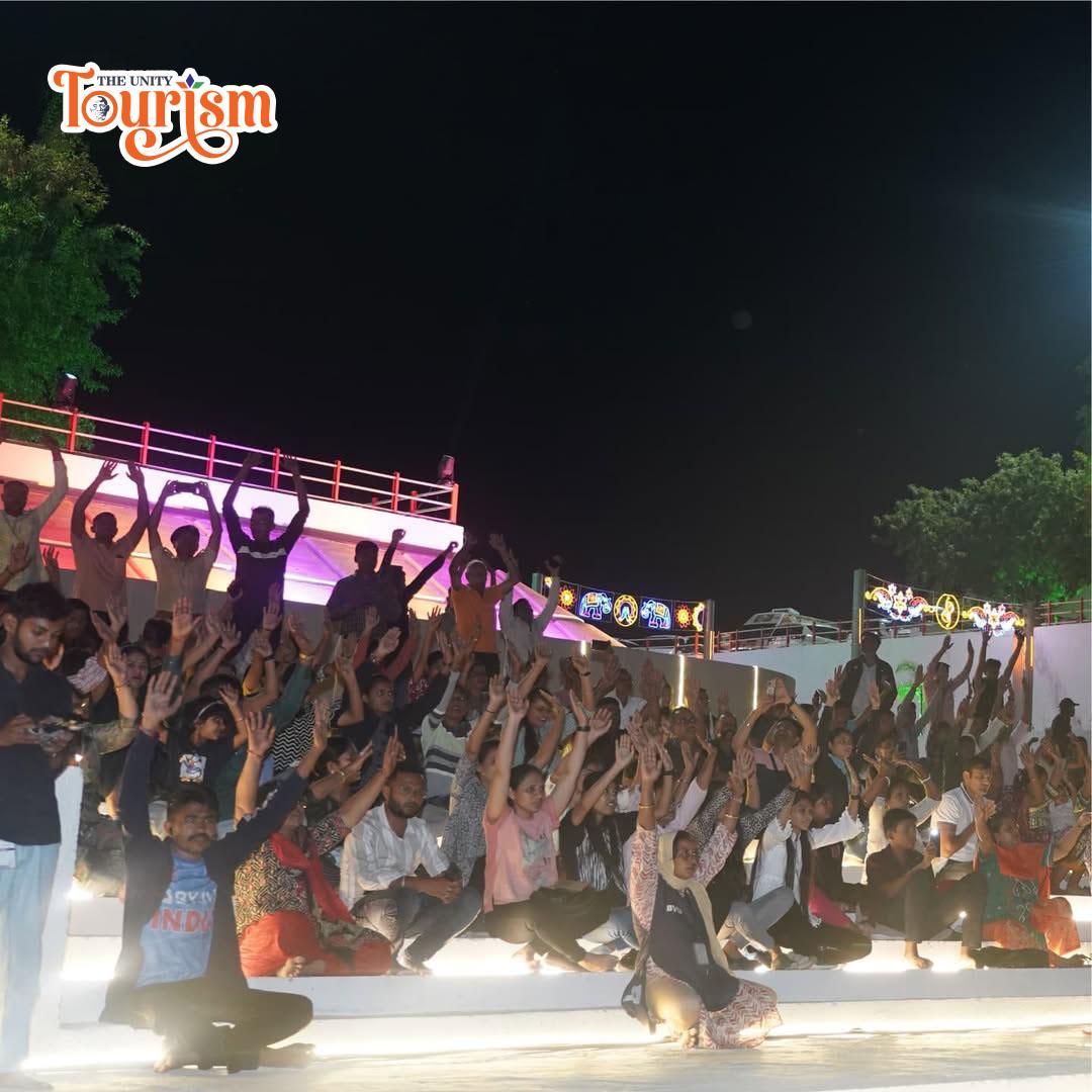 A night scene of individuals seated on steps, celebrating the Pooja at the River Front during the Narmada Maha Aarti.